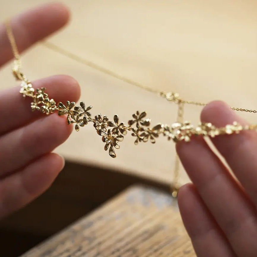 Gold necklace held between two hands with a blurred background