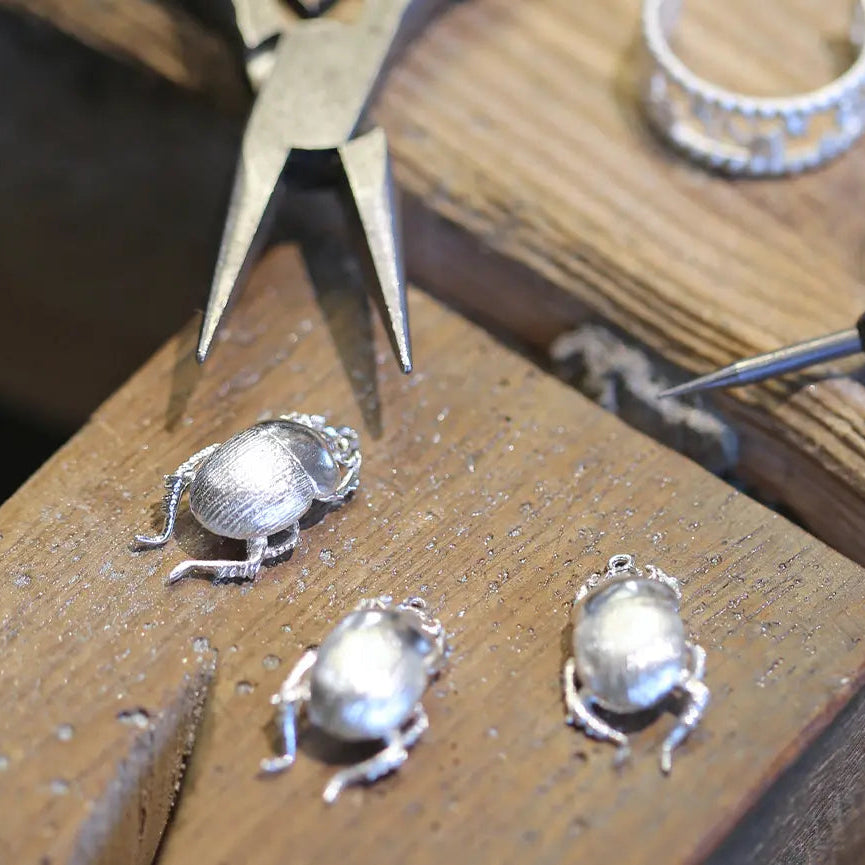 Silver beetle jewellery castings on a wooden workbench with tools.