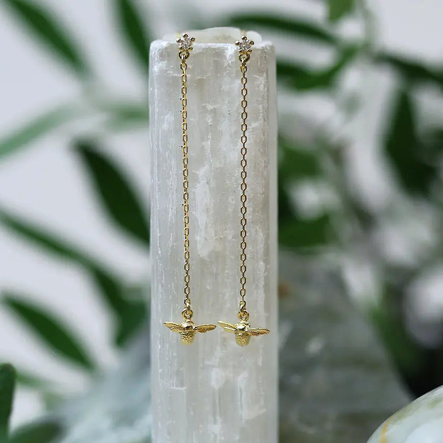 Gold bee earrings on a white stone with a natural background