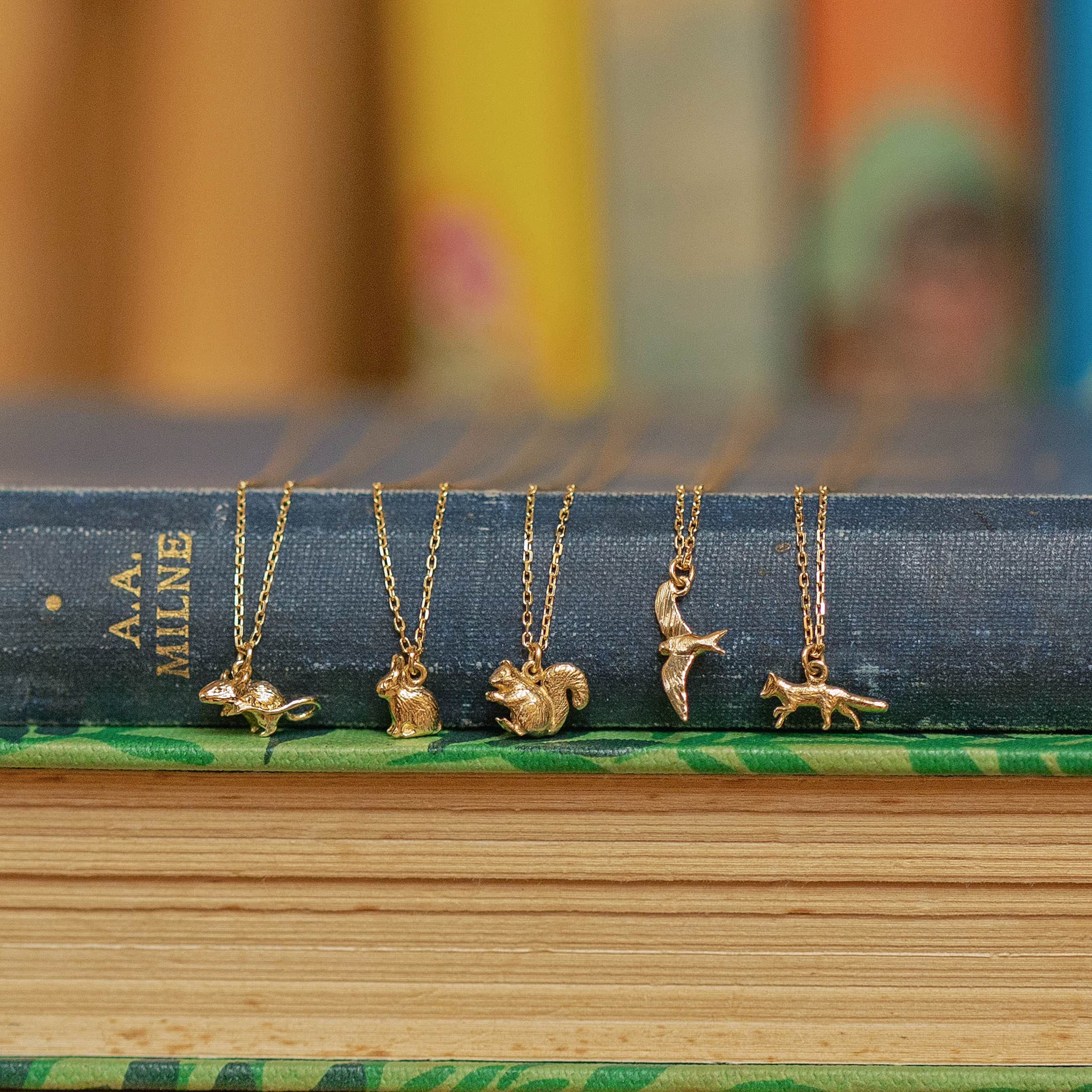 Collection of Alex Monroe miniature gold animal necklaces including fox, squirrel and bird charms styled on antique books