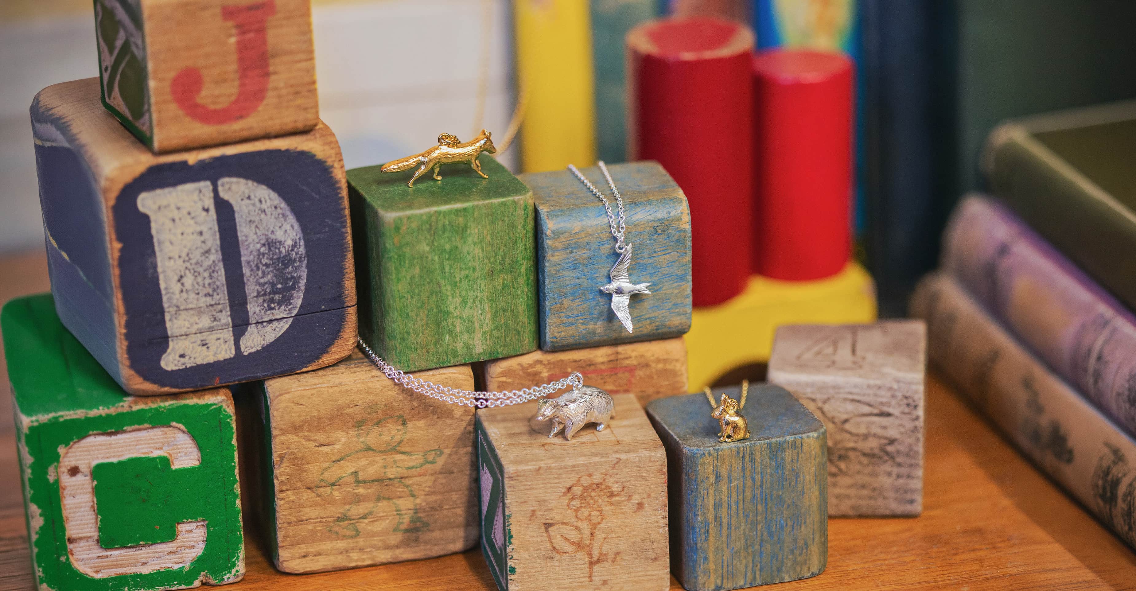 Handmade jewellery Gold and sterling silver animal charm necklaces including fox, bird and hedgehog pendants styled on colourful wooden toy blocks