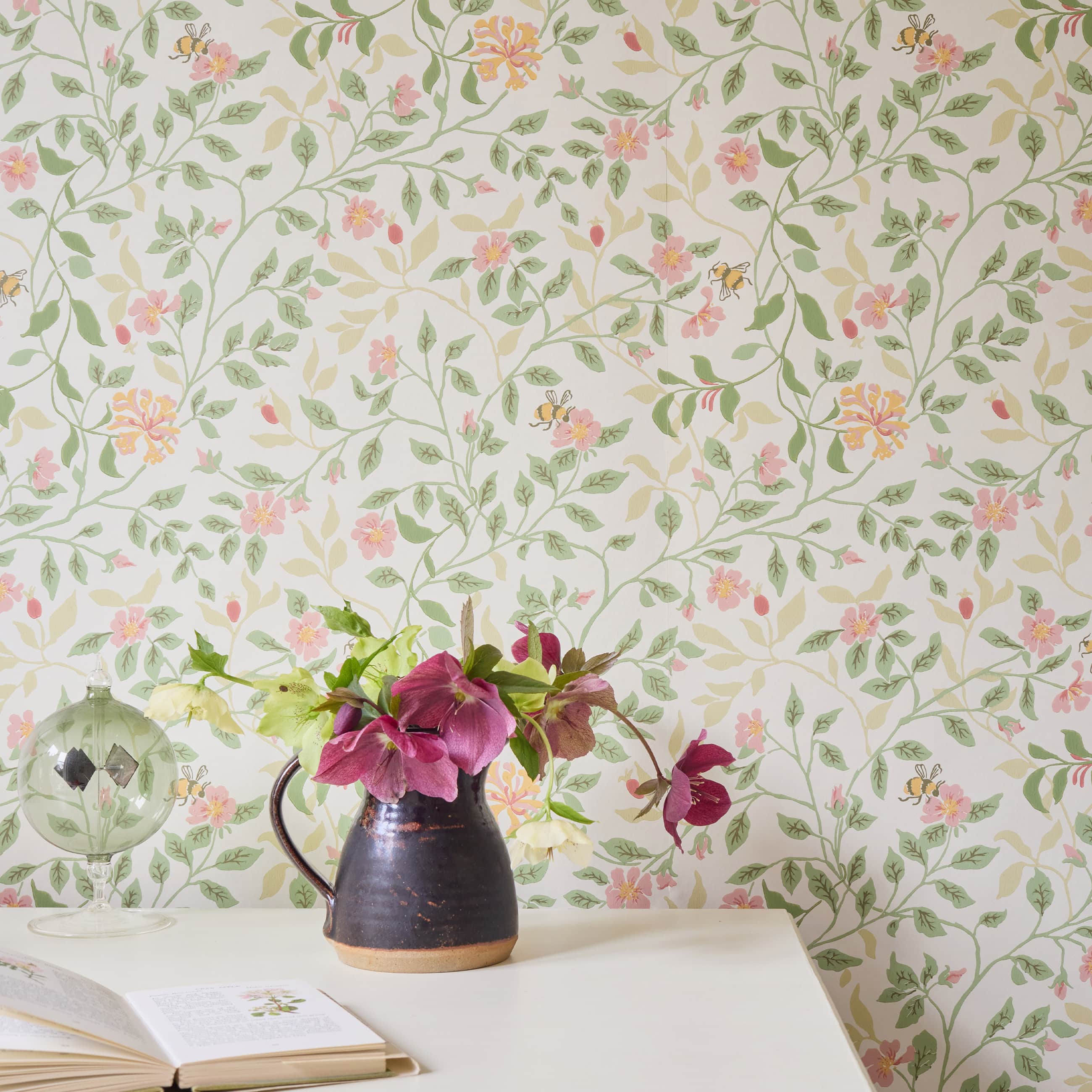 Delicate floral wallpaper with trailing greenery and soft pink blooms, styled with a rustic vase of fresh flowers, an open book, and gathered objects